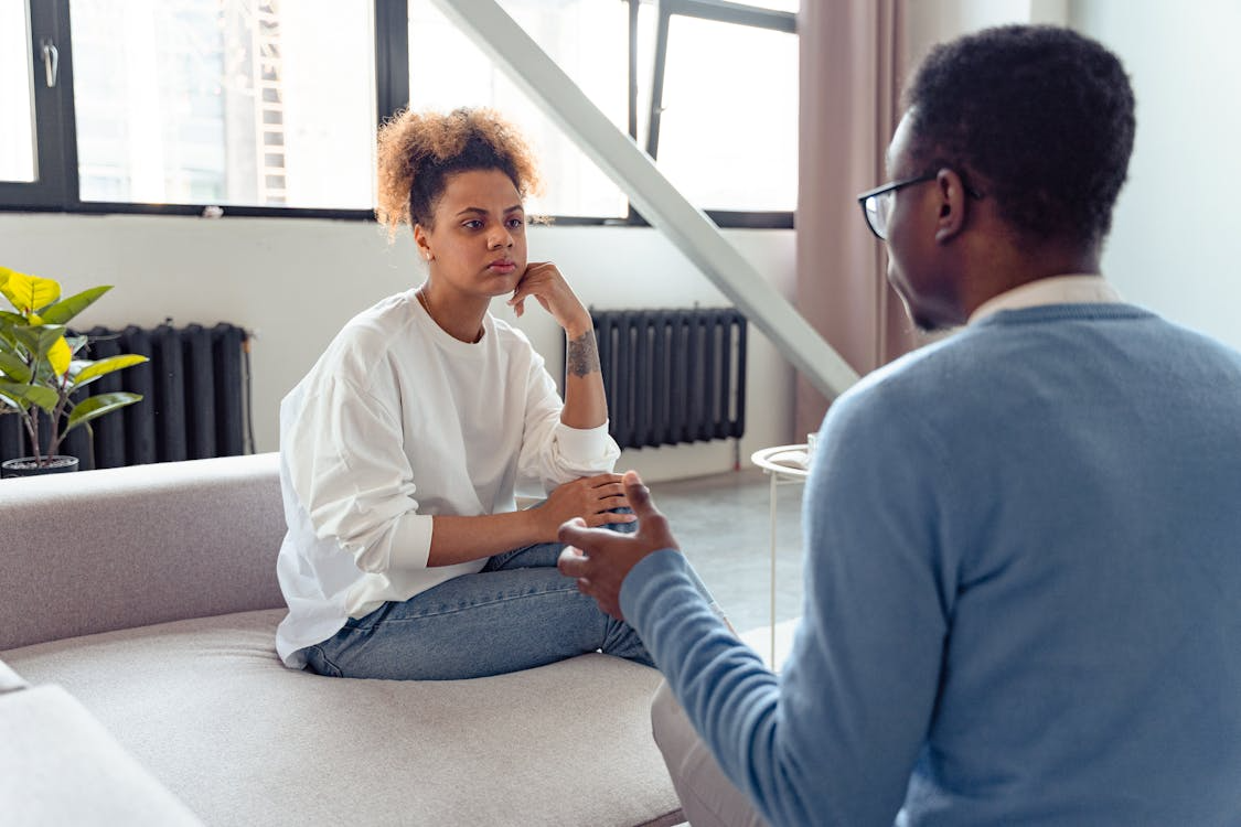a woman sitting on a sofa opposite a man who is talking to her