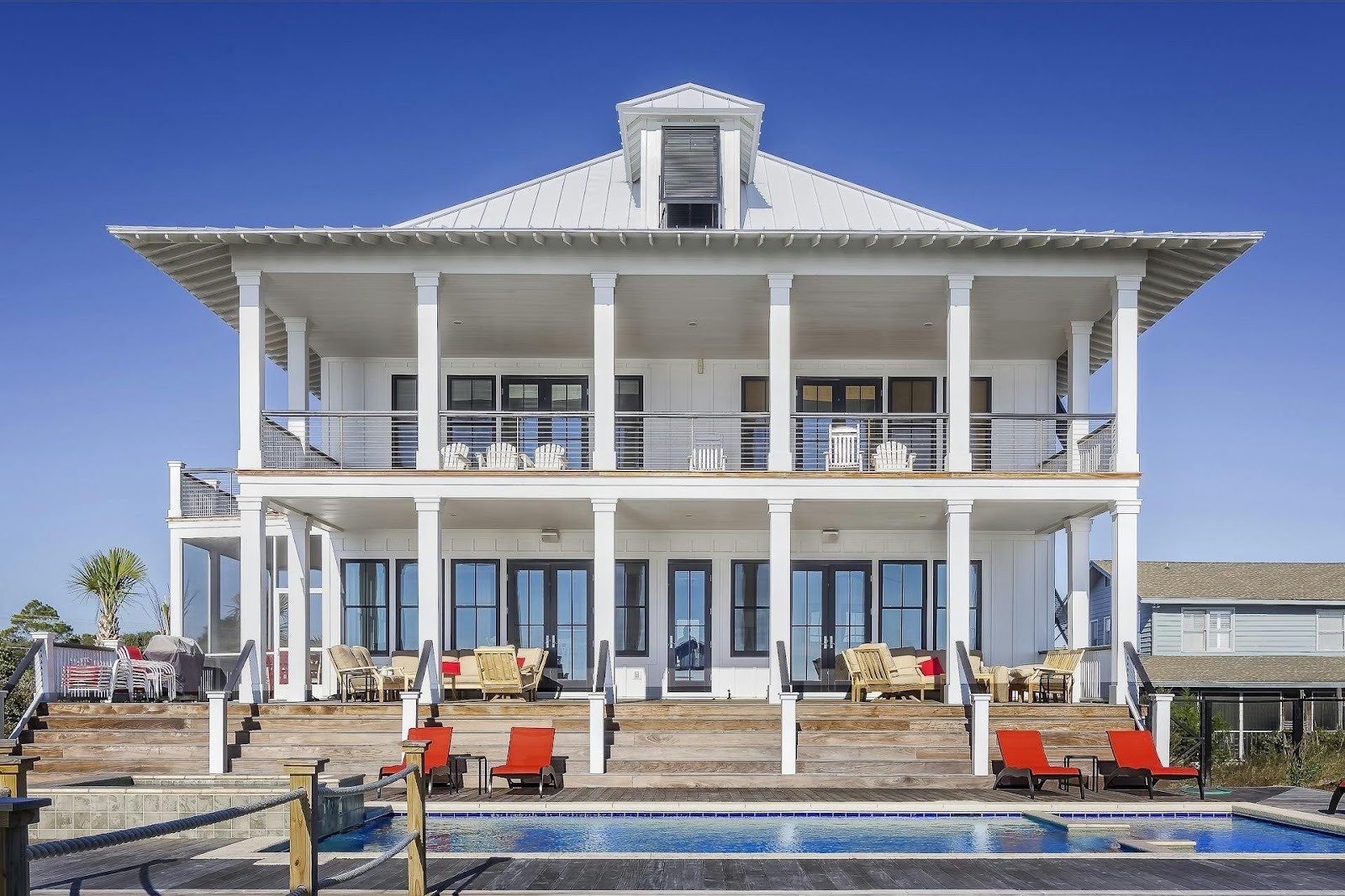 big white house with columns and red sunbeds in front of it, next to pool
