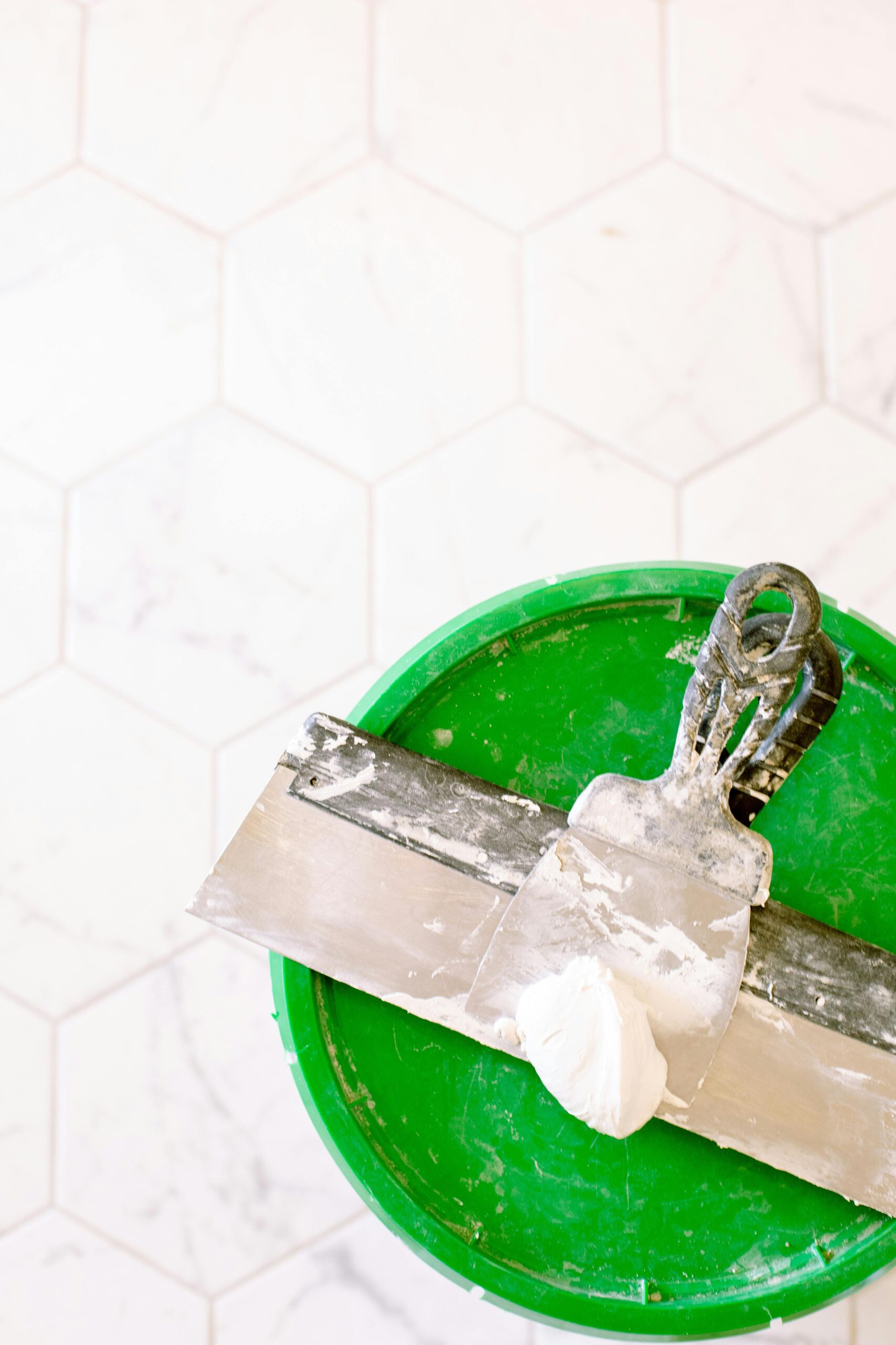 green lid with plaster scraper sitting on top of it on floor tiles