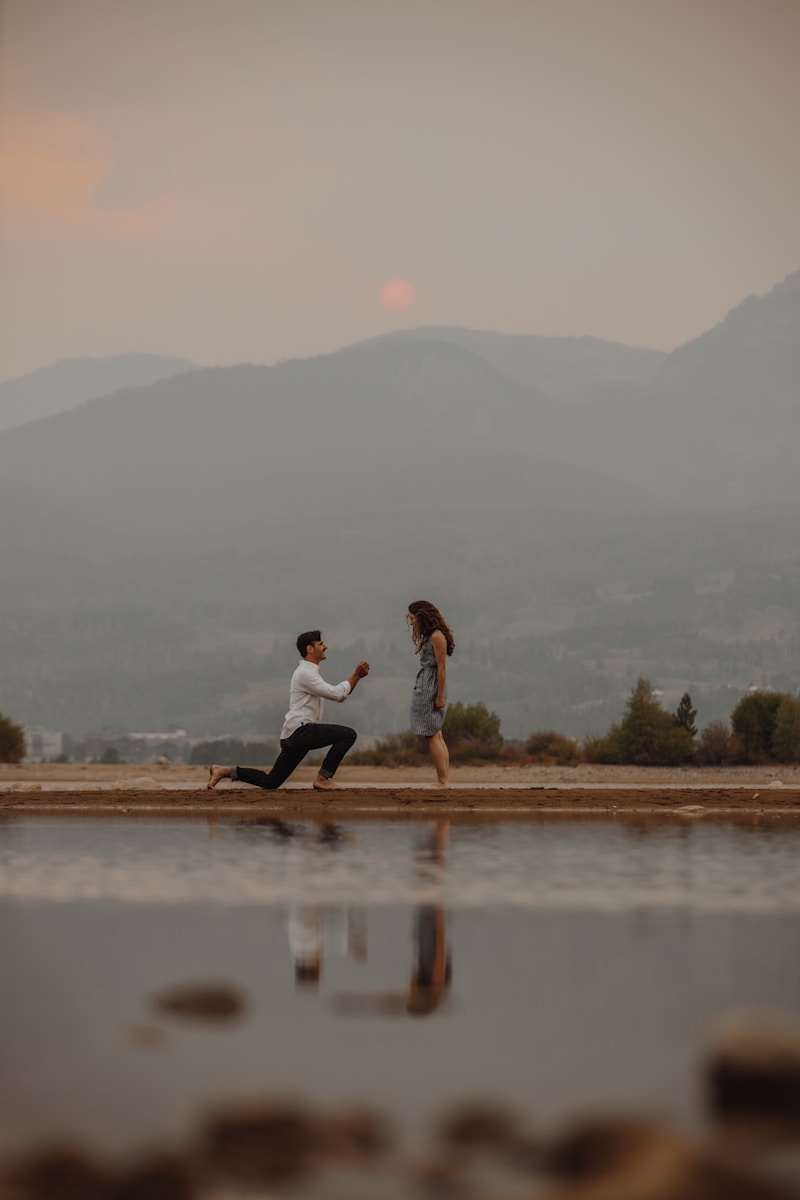man in white shirt and black pants crouching down in front of woman and proposing to her during daytime