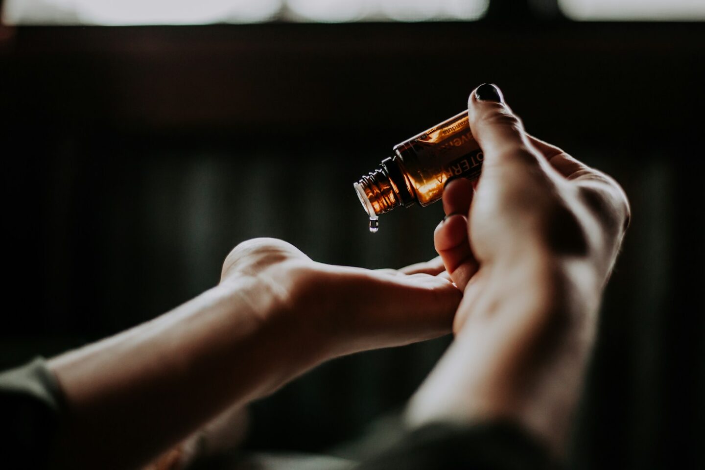 person holding amber glass bottle of oil and dripping it into palm of hand