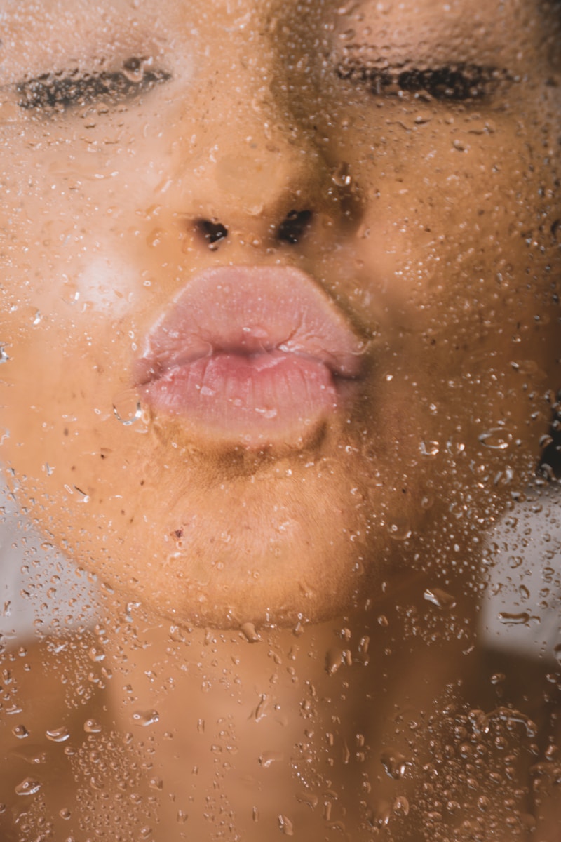 woman pursing her lips up against a clear screen with water droplets on