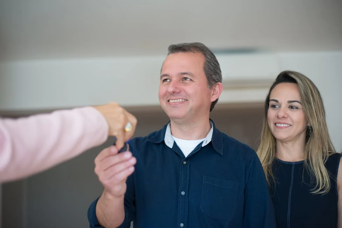 woman standing next to man in house, who is taking a key from another person's hand