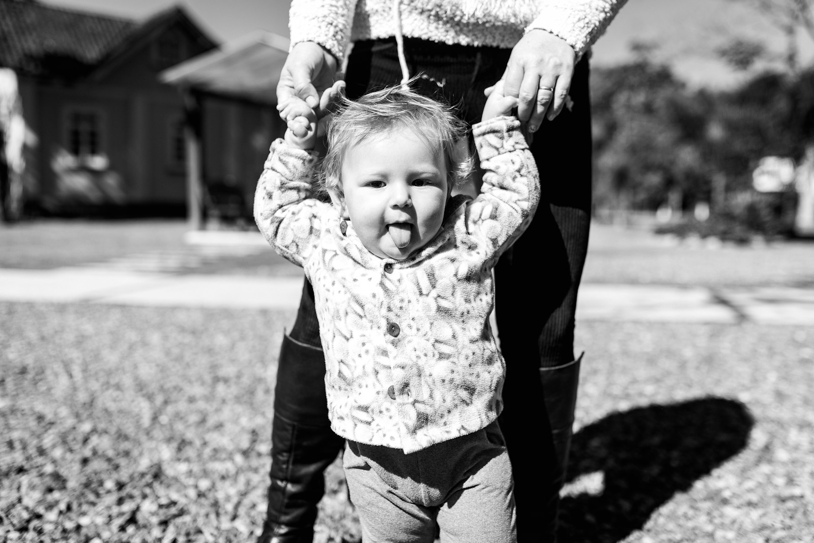 grayscale photo of young child in long sleeve shirt and denim jeans and holding hands with adult above them