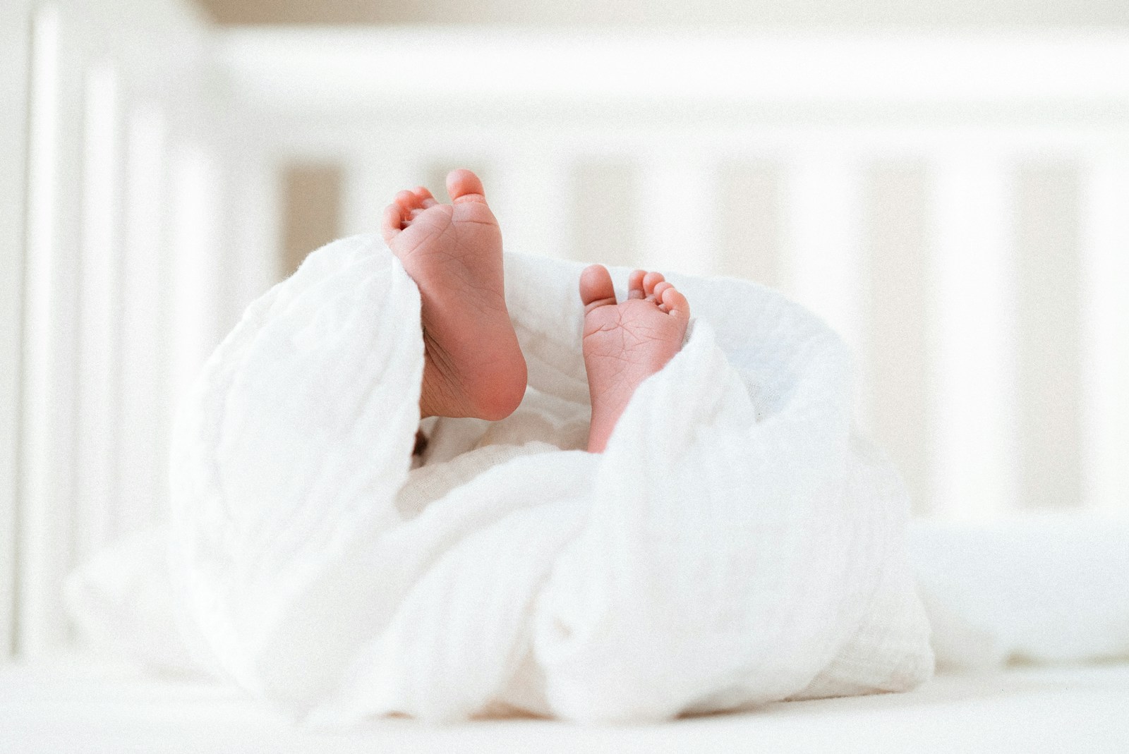 small baby covered with white muslin in cot