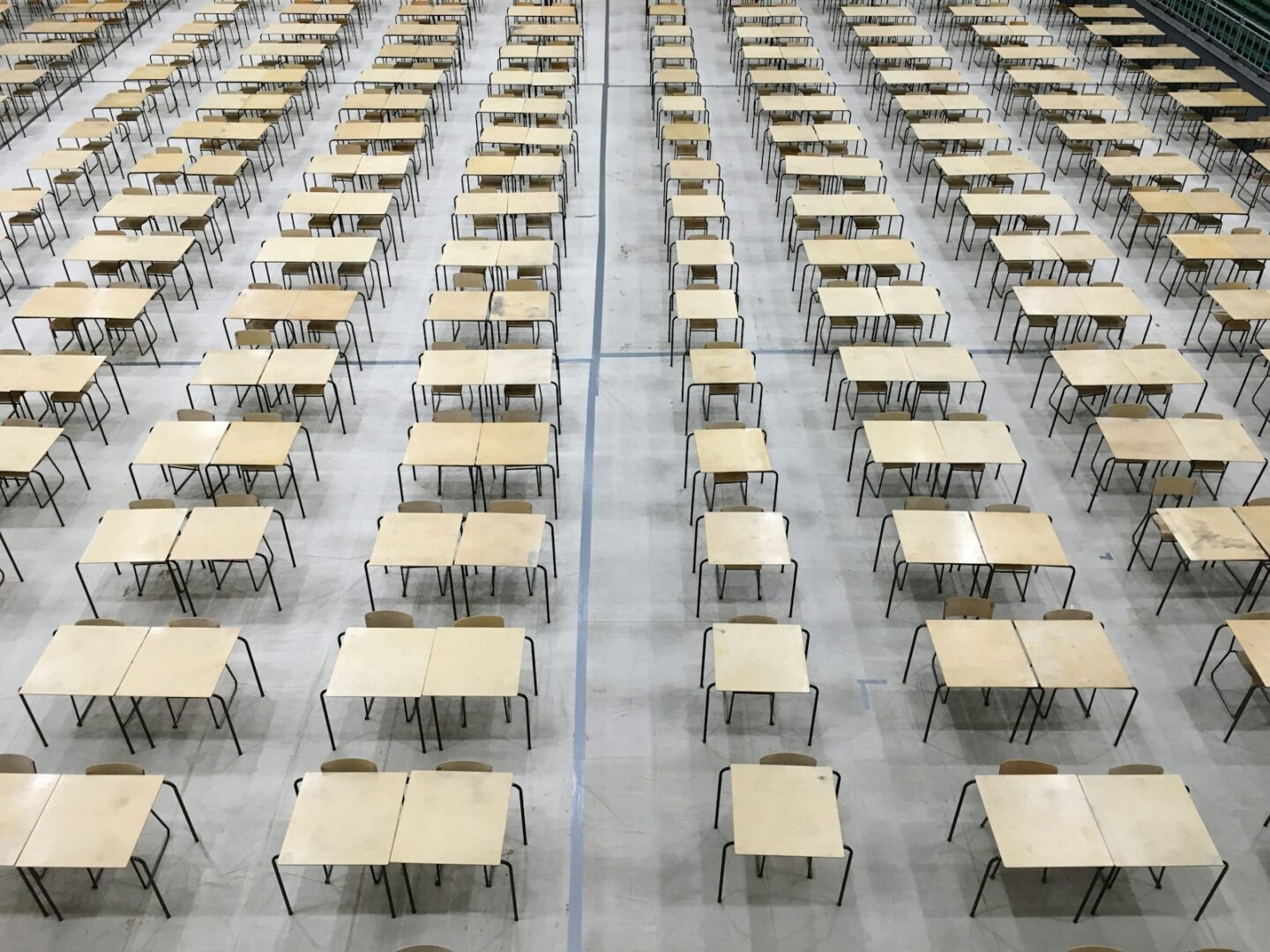 many wooden desks and chairs set up for exams in school hall