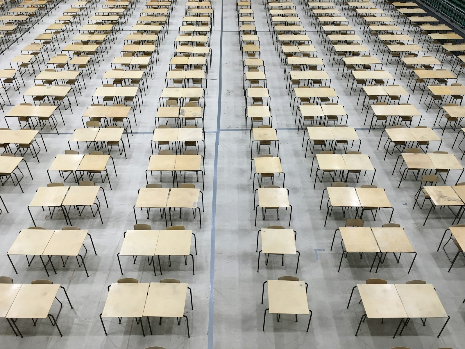 many wooden desks and chairs set up for exams in school hall