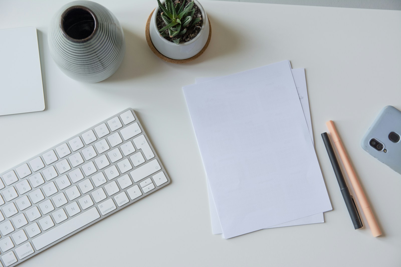 pile of white paper beside white apple keyboard, pen and plants