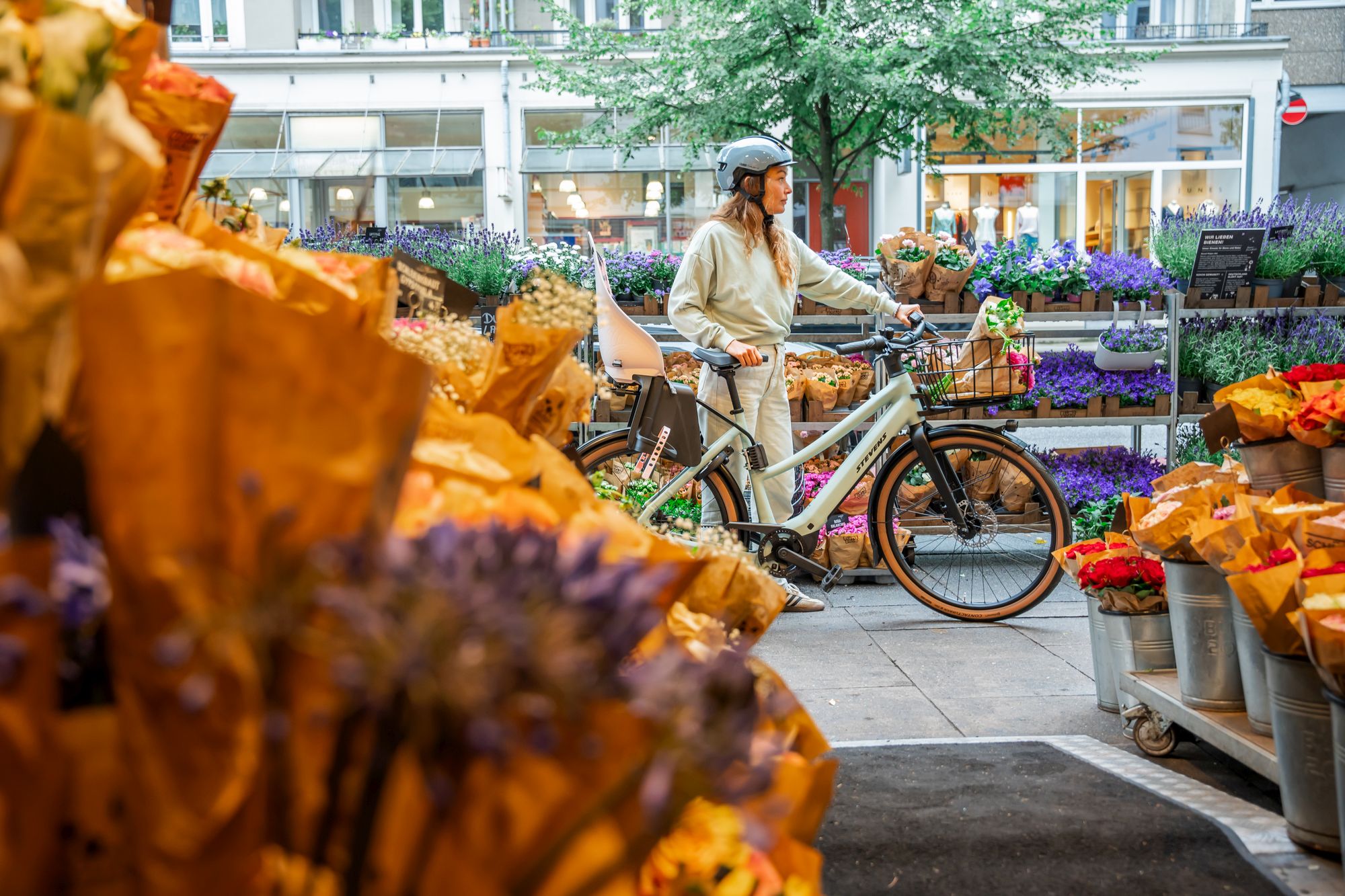 woman wearing a helmet and holding a bike in the middle of an outdoor flower market