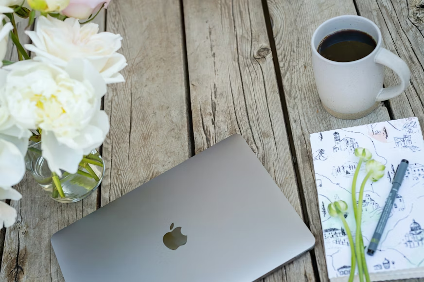 laptop on wooden table next to flowers