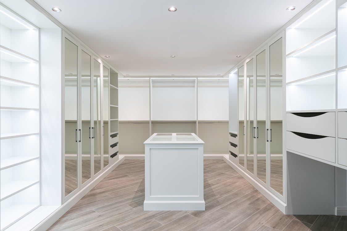 walk in wardrobe with mirrored doors along sides and white unit in centre of room