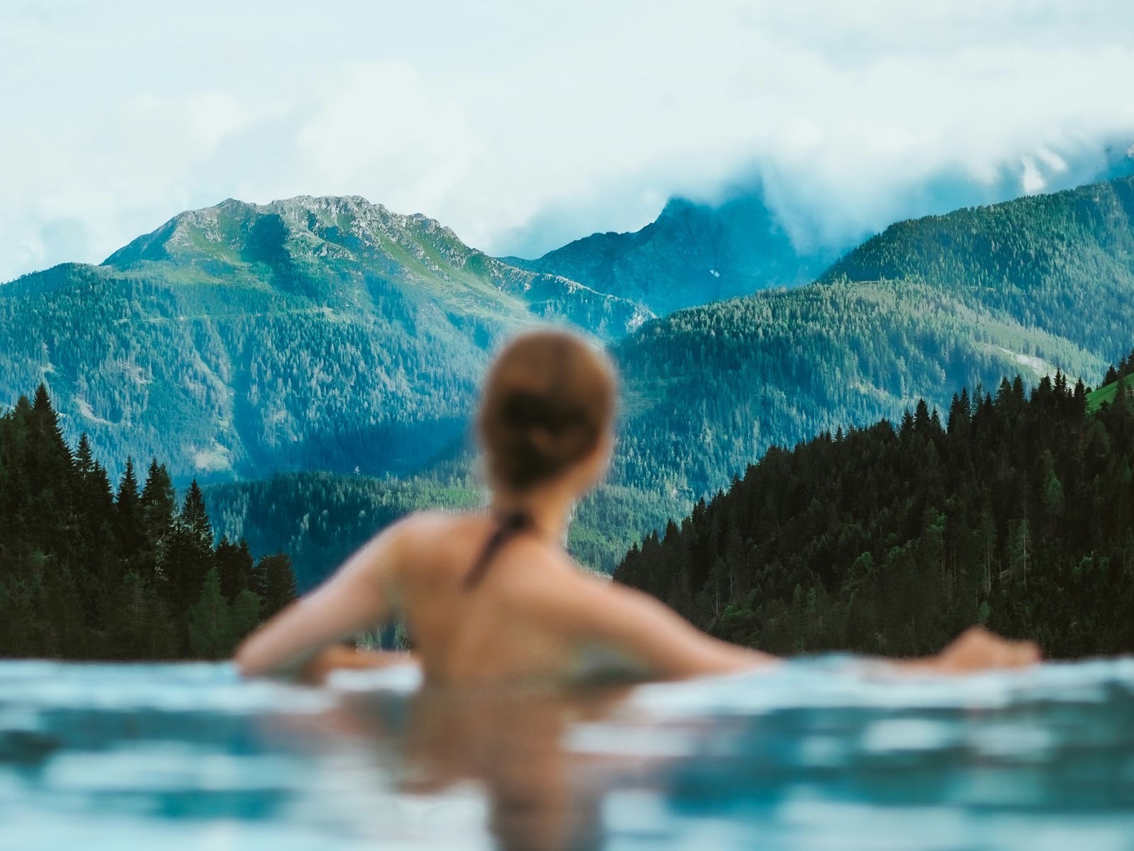 woman from the back in an outdoor pool with mountains in the distance
