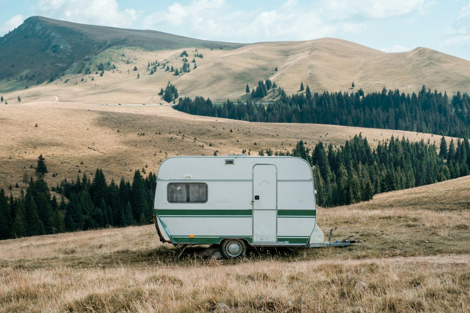 white and green caravan on brown grass field and hills in the distance