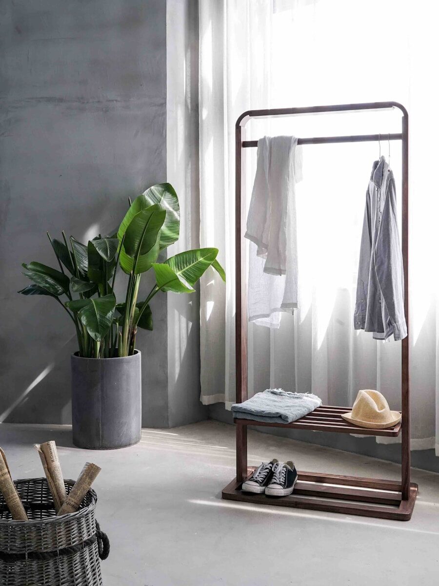 grey dress shirt hang on brown wooden rack in front of window with white curtain