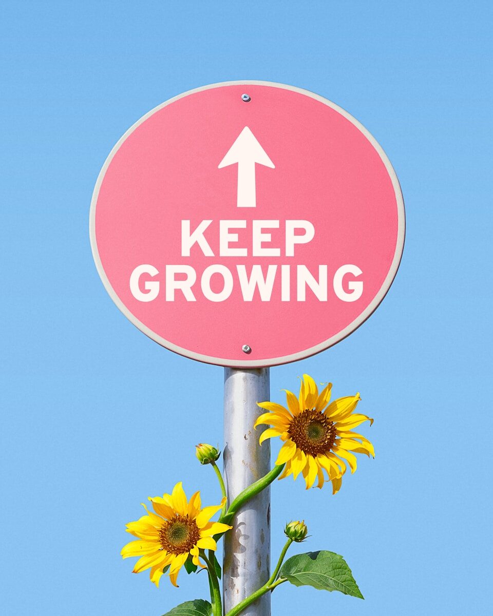 Pink sign with "keep growing" and sunflowers against blue sky