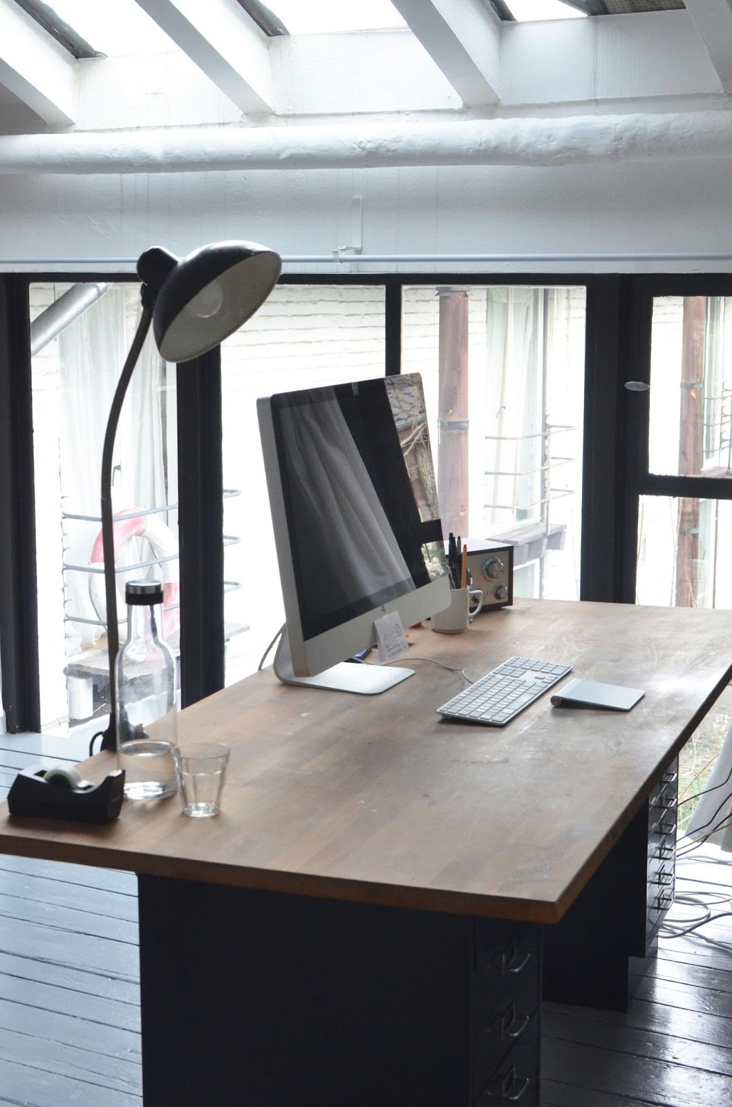 wooden desk with a large computer monitor on it and a tall lamp, keyborard water and stationery