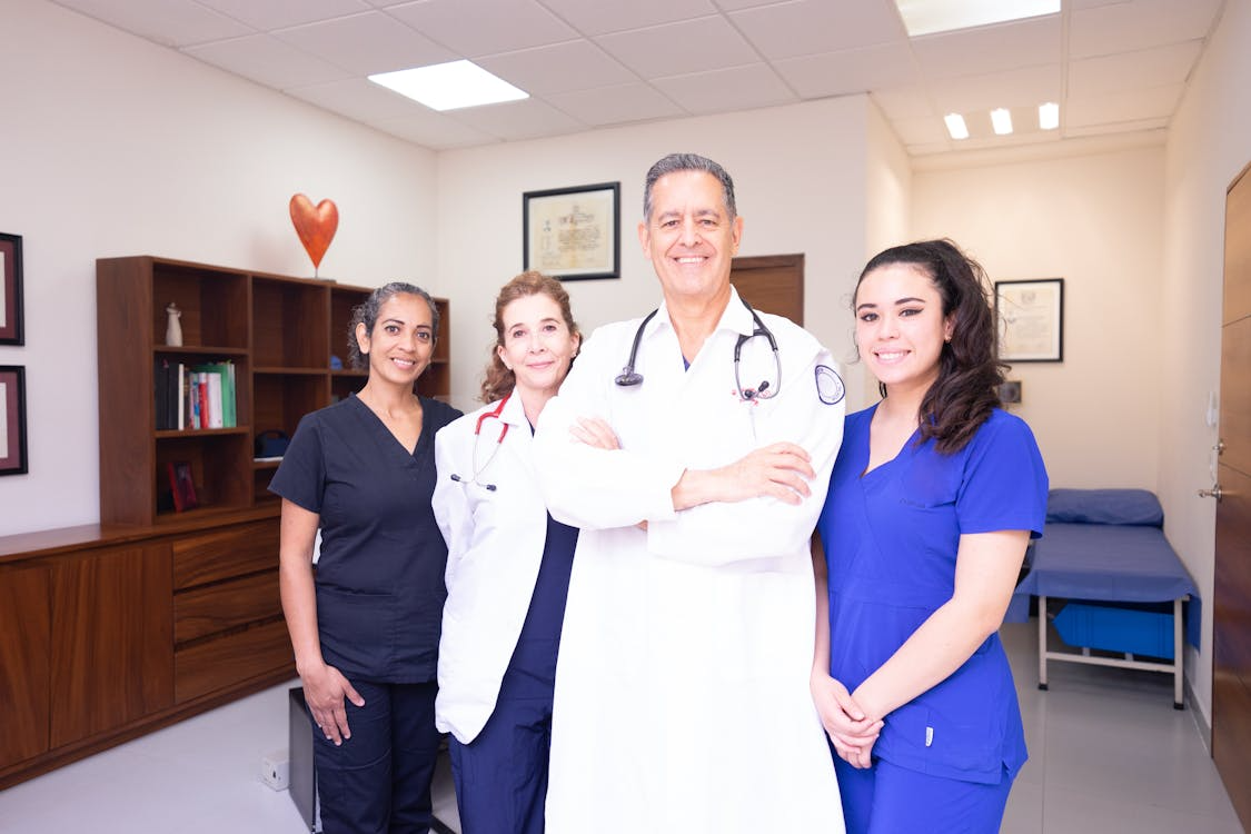 three woman and a man wearing doctors and nurses uniforms, standing next to each other and smiling