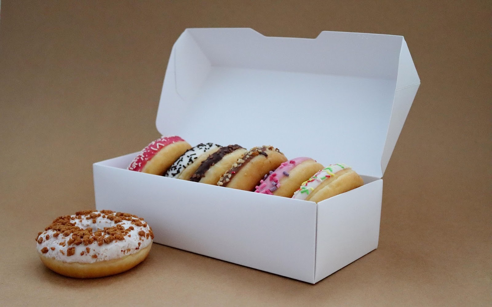 iced doughnuts in a white box with one sitting next to it