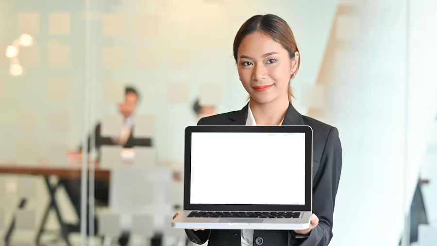 women in suit smiling and holding an open laptop facing outwards with a blank white screen