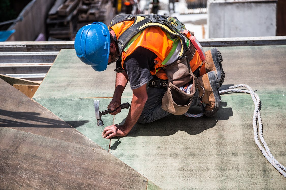 workman in hi-vis jacket and blue hard hat hammering something into ground