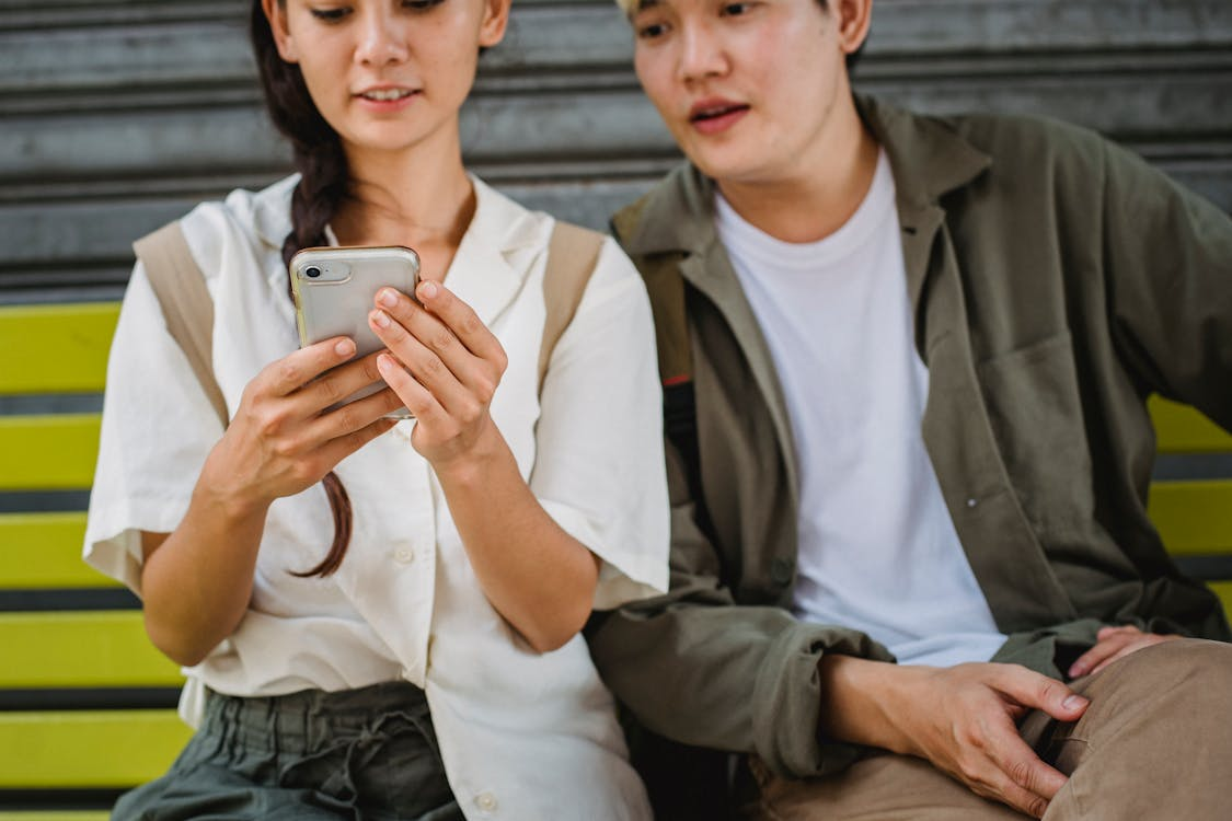 man and woman sitting on steps, and both looking at phone woman is holding