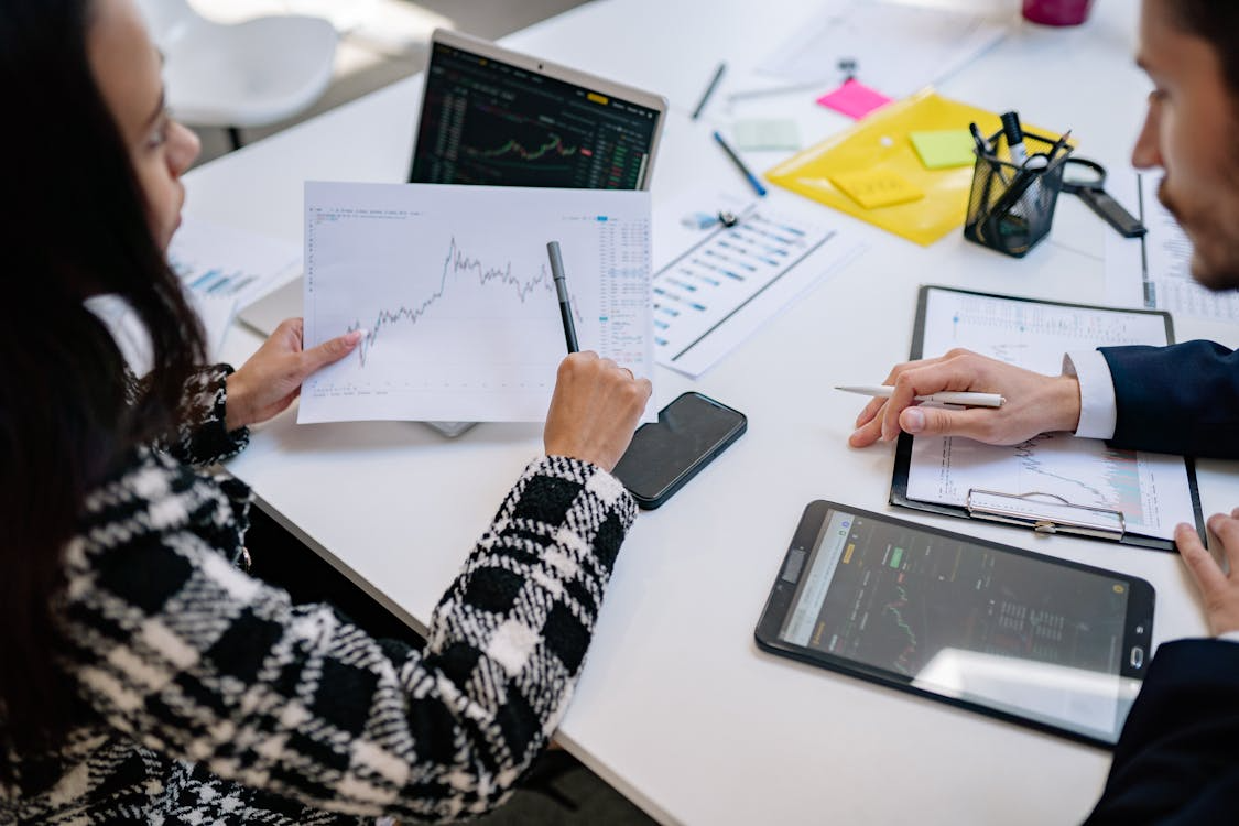 man and woman sitting on desk looking at papers with graphs on
