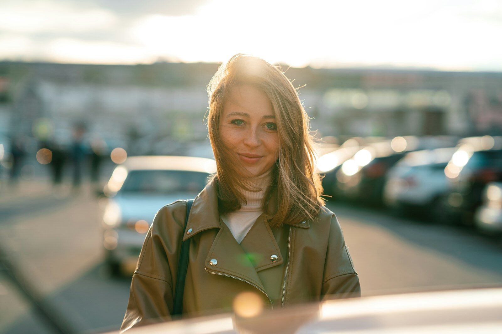 a woman in a green jacket, outside on street, facing the camera and smiling