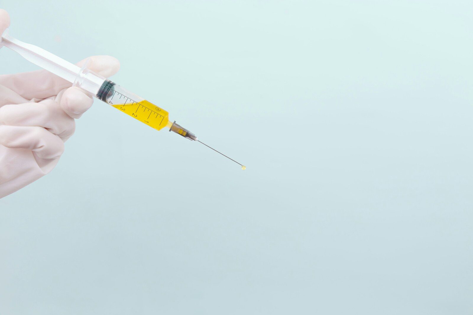 person's hand in white surgical gloves holding needle with yellow liquid in it