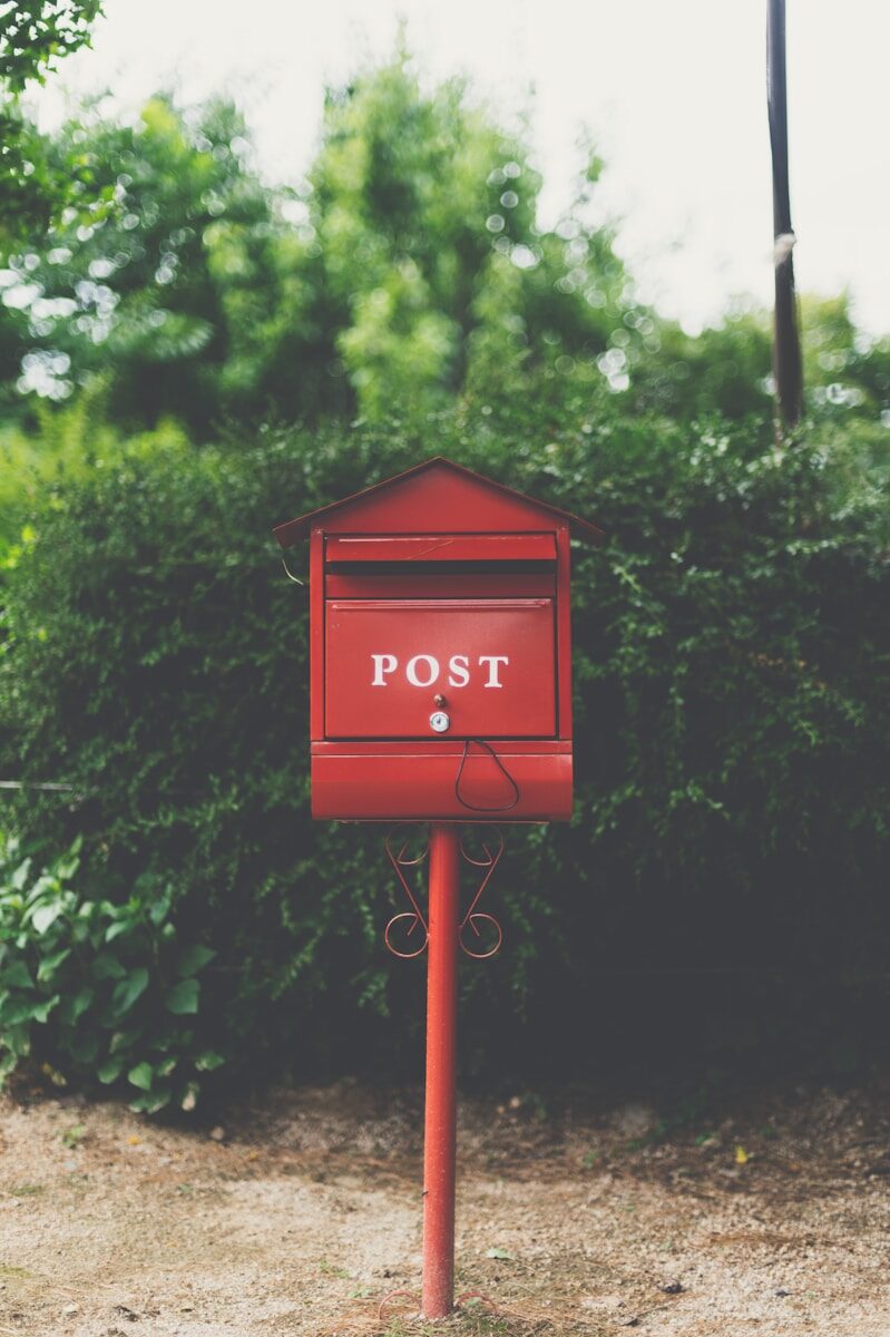 red wooden postbox in front of green bush