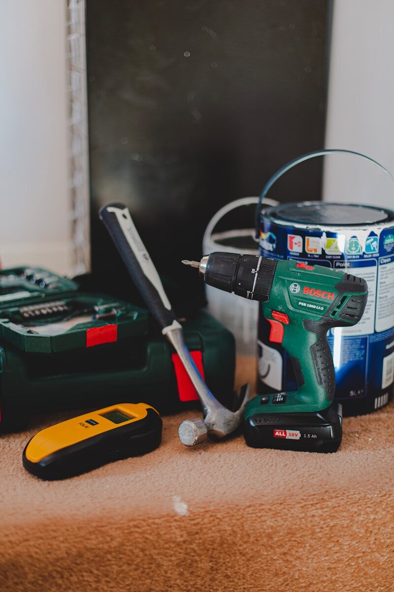 cordless power drill beside hammer and other tools on floor