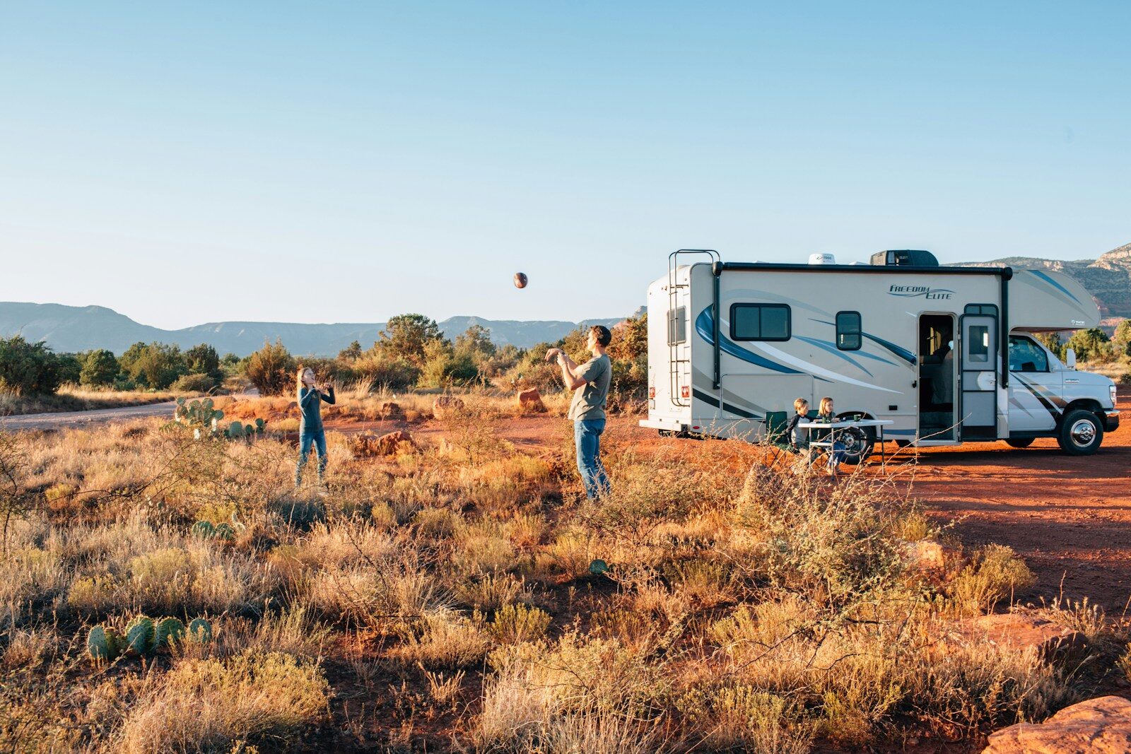 family playing catch with ball next to motorhome on brown grassy land
