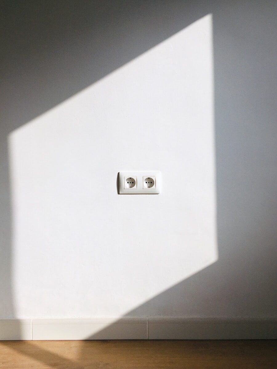 a double plug socket in a white room with a shadow on the wall and sun shining onto it