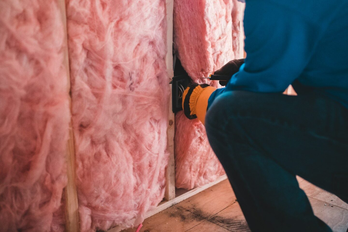 person crouching down in house and installing pink insulation