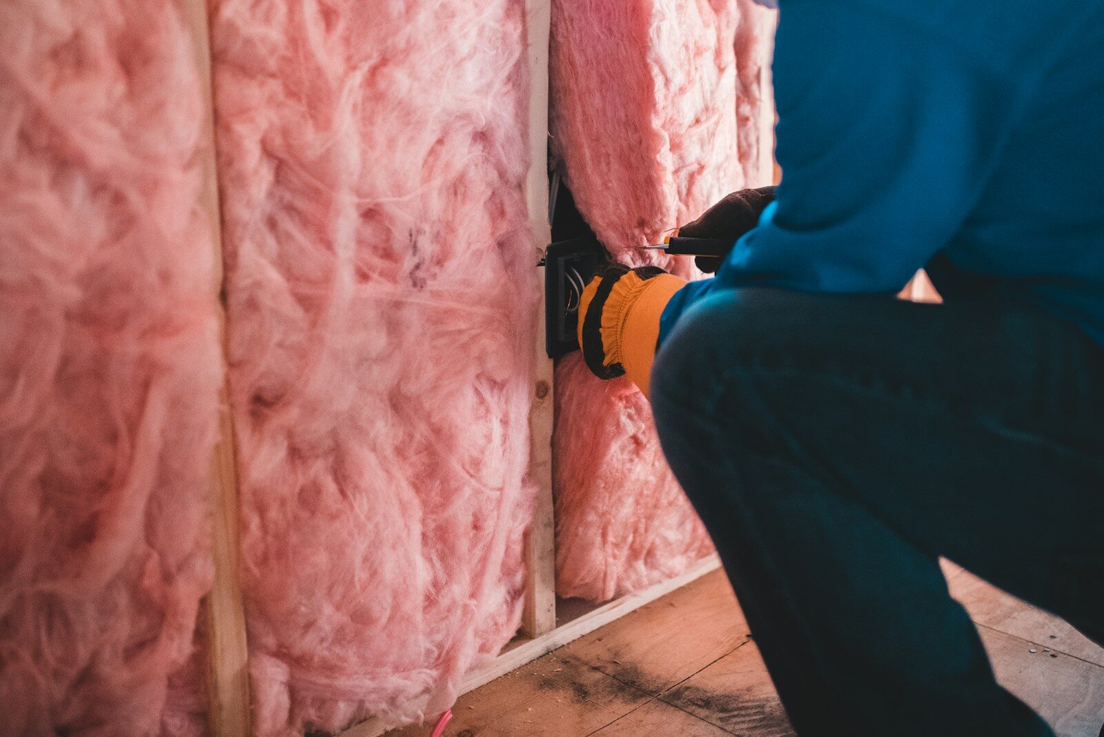 person crouching down in house and installing pink insulation