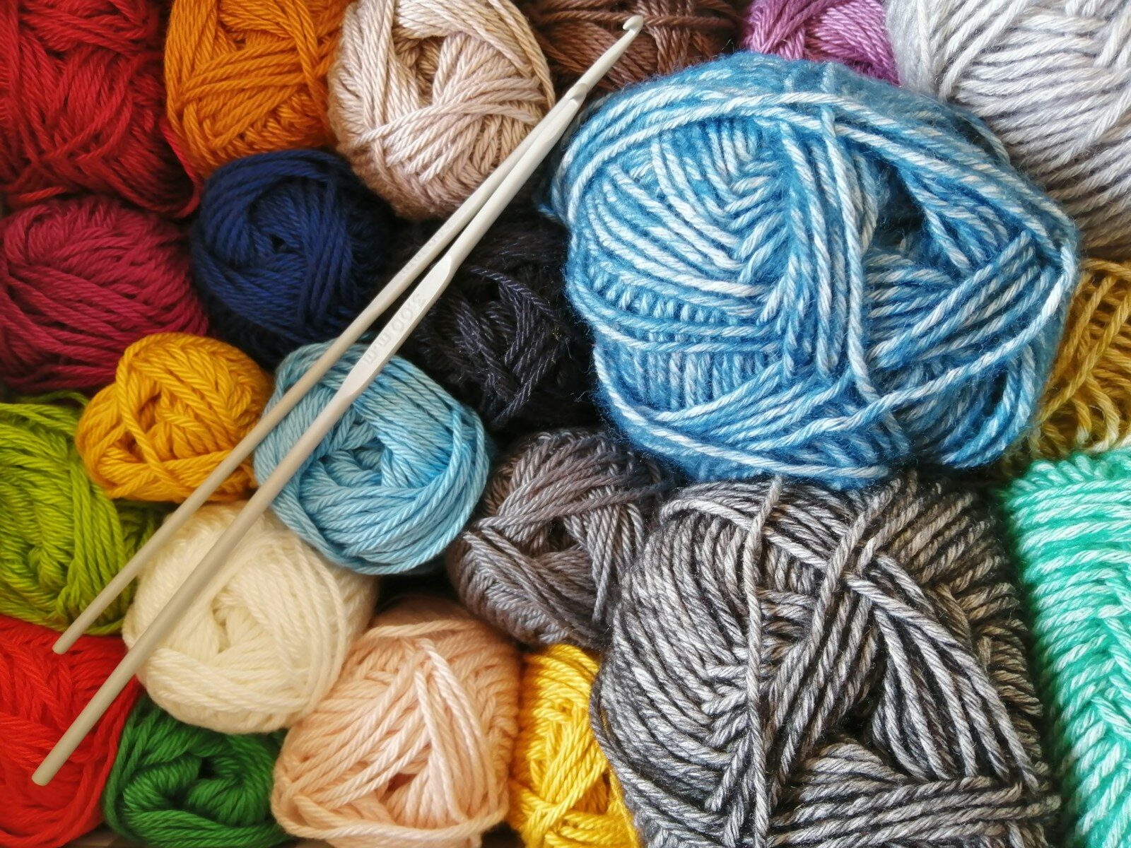 coloured yarn in pile with knitting needles across them