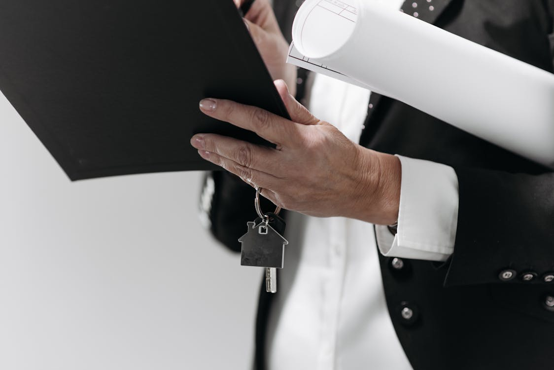 person holding black folder and keys with house-shaped key ring on them