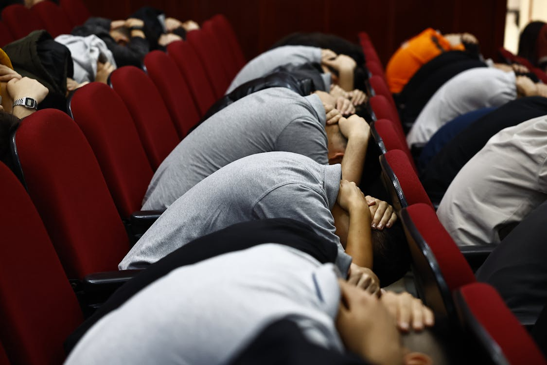 rows of people sitting down with heads forward under arms in brace position