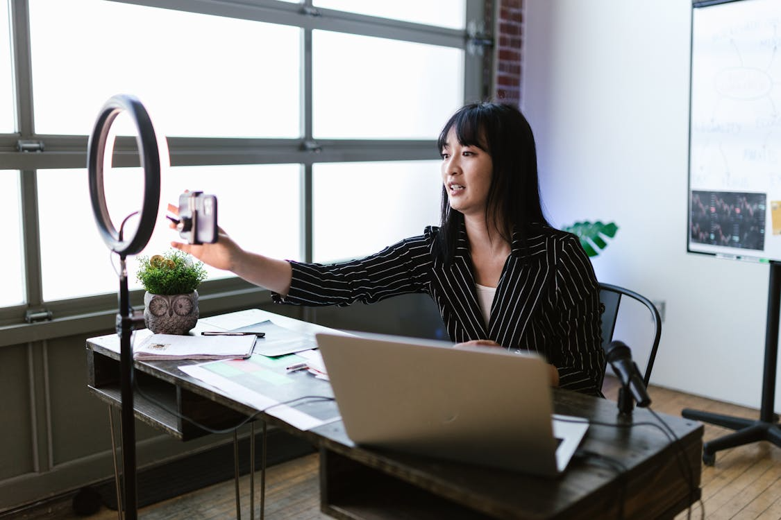 woman sitting at desk with phone attached to ring light
