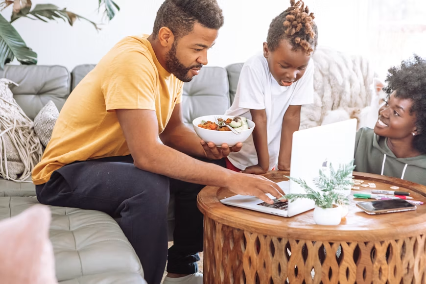 family sitting around laptop on coffee table in living room