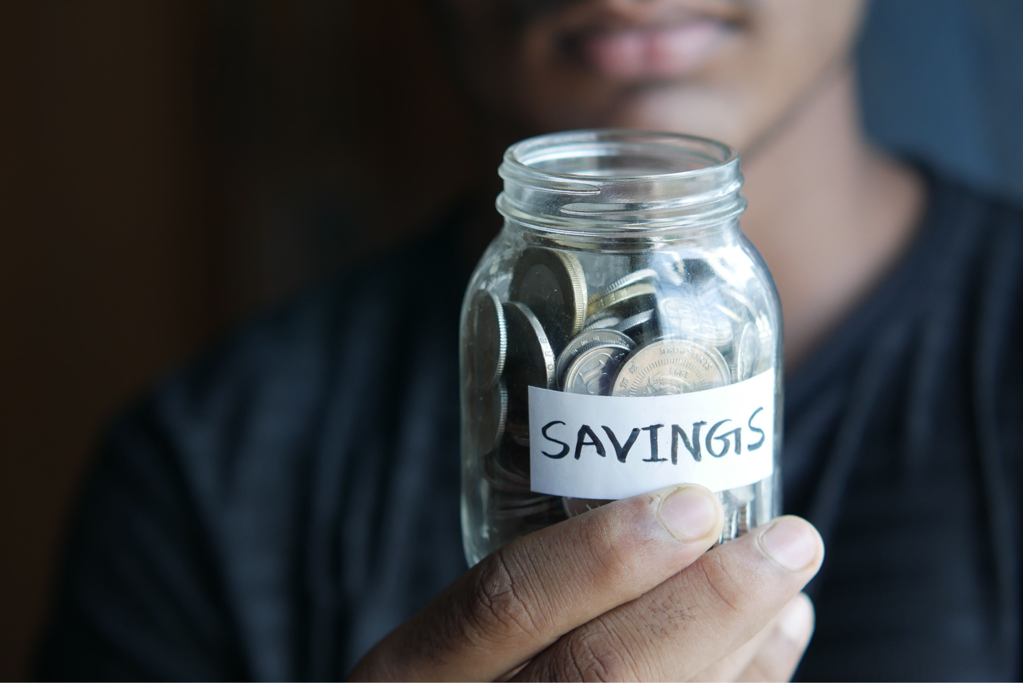 person holding glass jar full of coins with a label saying 'savings'
