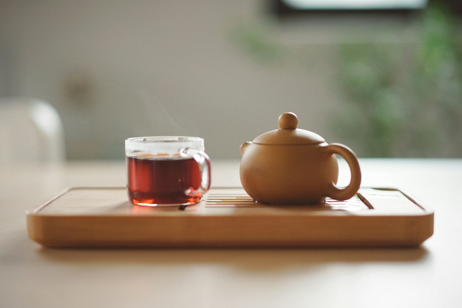 clear glass cup with tea in next to brown ceramic teapot