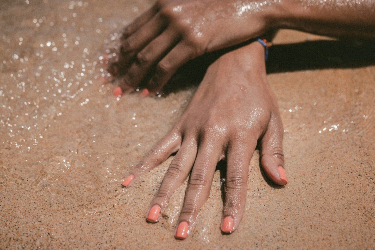 persons hands  in sea water on the sand showing nail polish