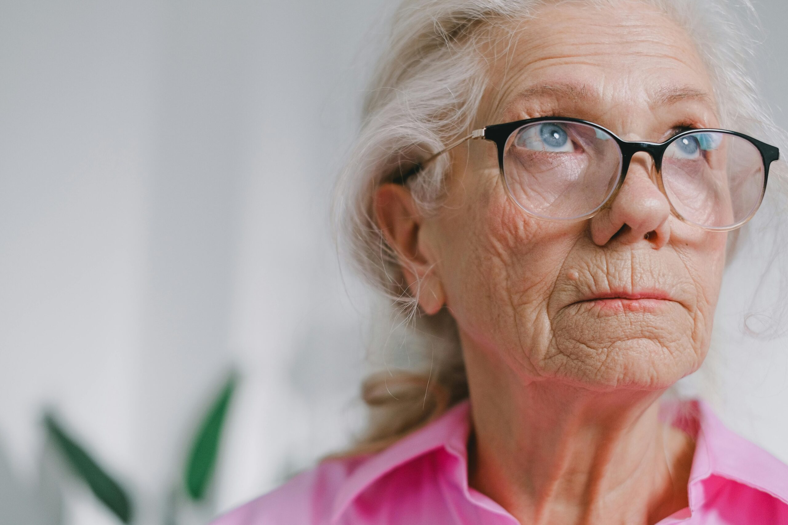 older woman wearing glasses and pink top looking up