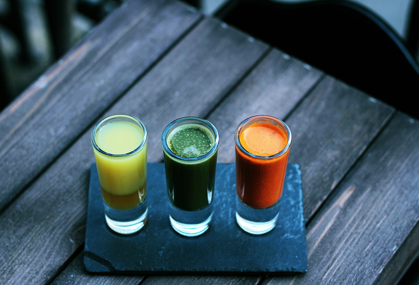 three clear shot glasses witih different coloured liquids in them