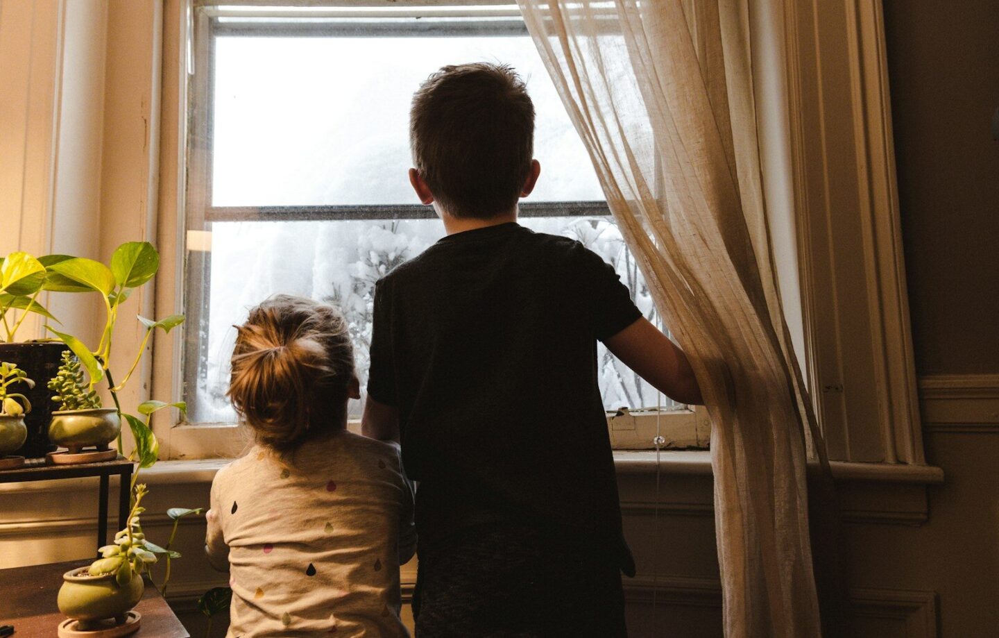 boy and girl standing near window at home looking outside