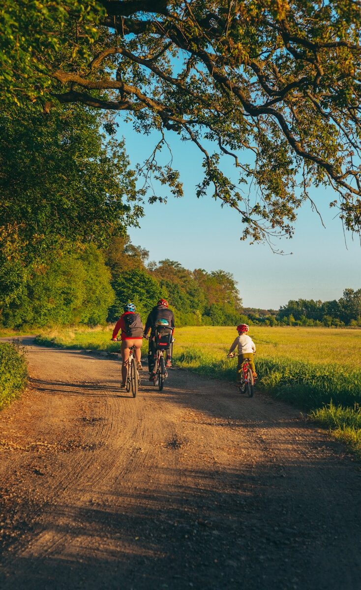 a family of three riding bikes down a path next to trees and a field