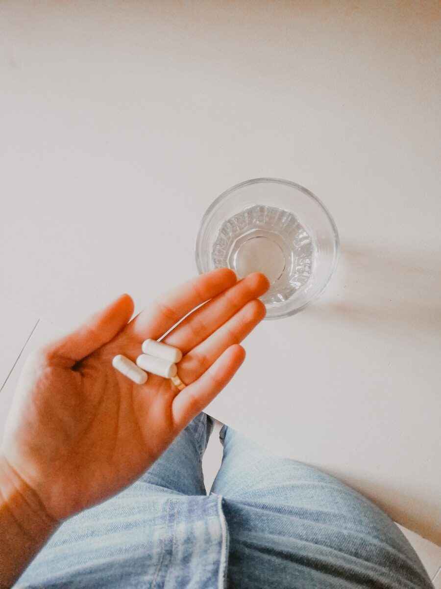person holding white pills above glass of water