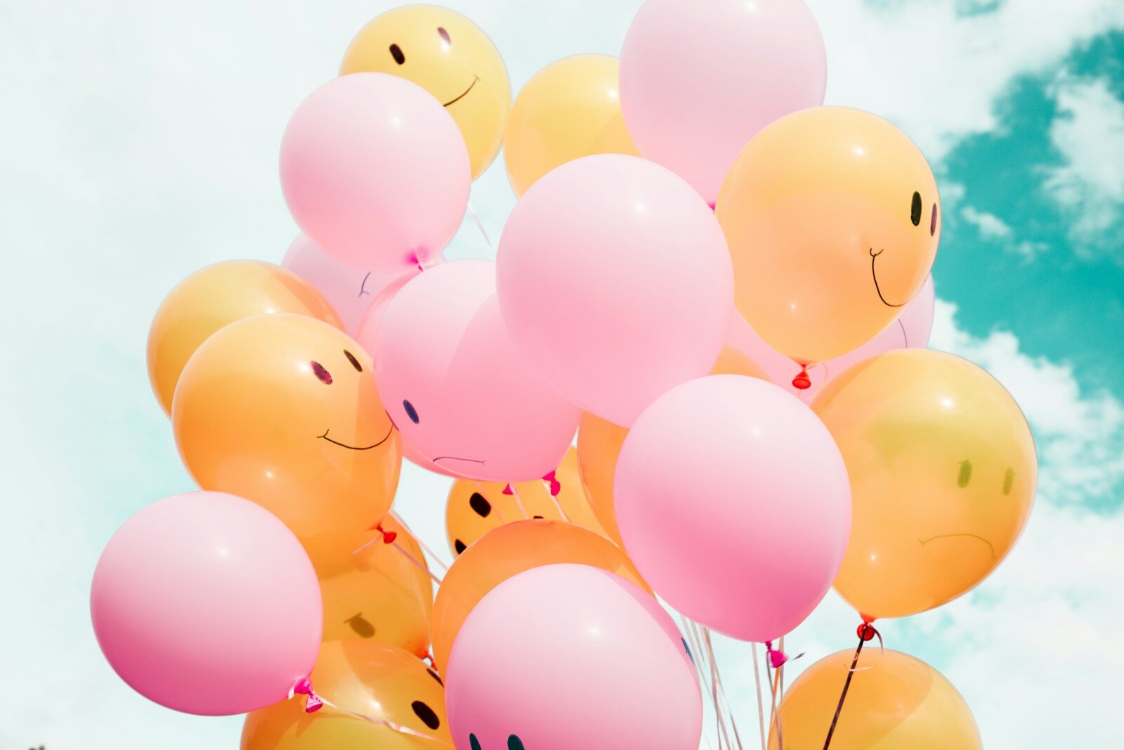 low-angle photo of pink and orange balloons with smiley faces on