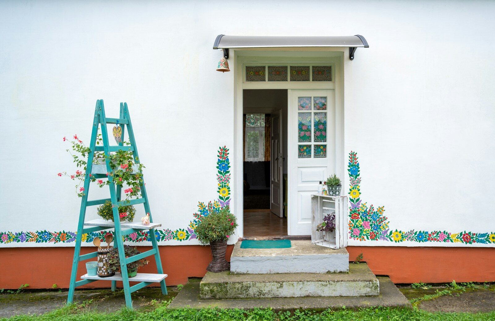 front of white house with blue ladder and plants in front of it