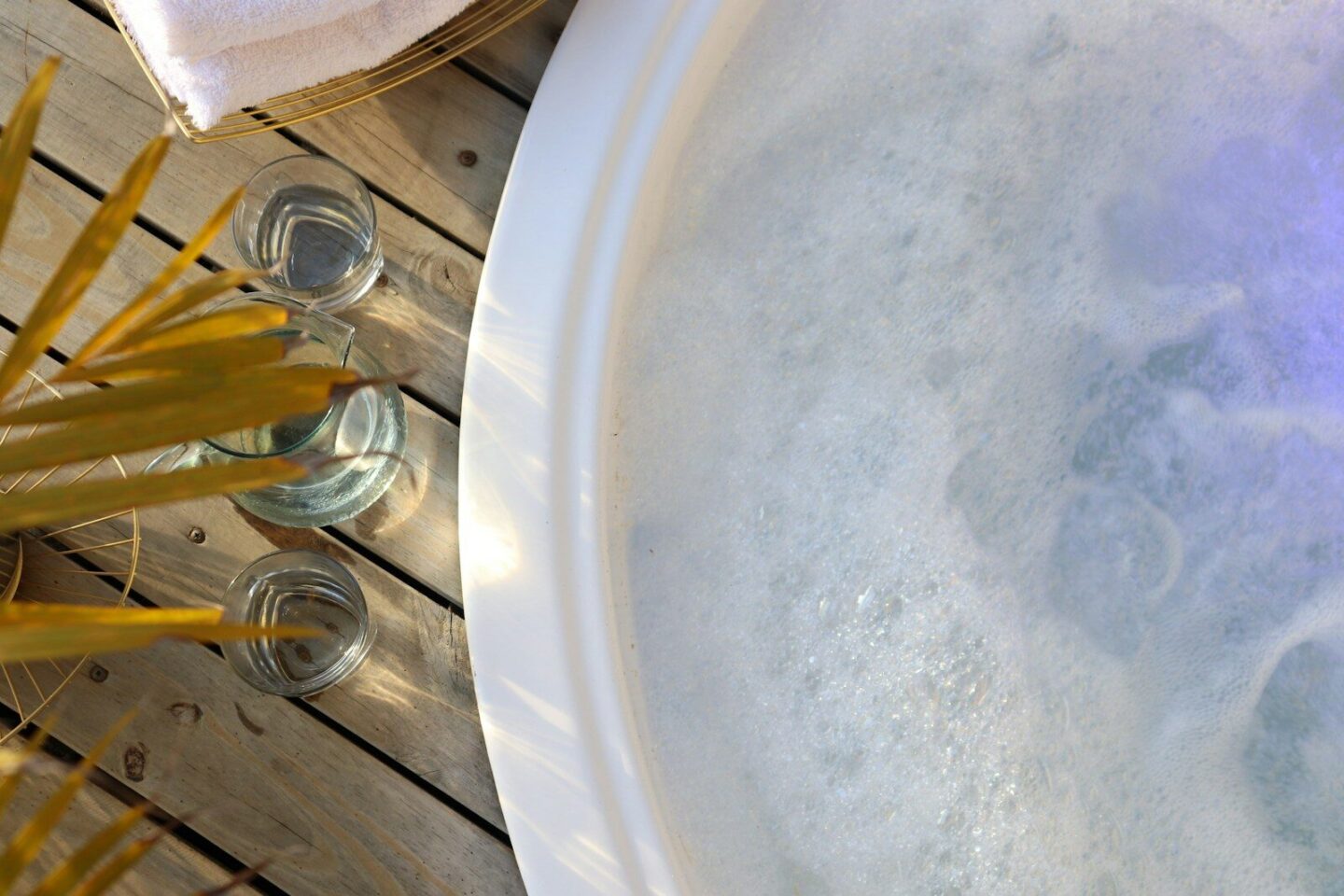 a hot tub with water from above, next toglasses of water on wooden decking